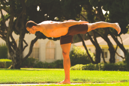 Man performing traditional Warrior 3 Pose with arms extended backward in a park