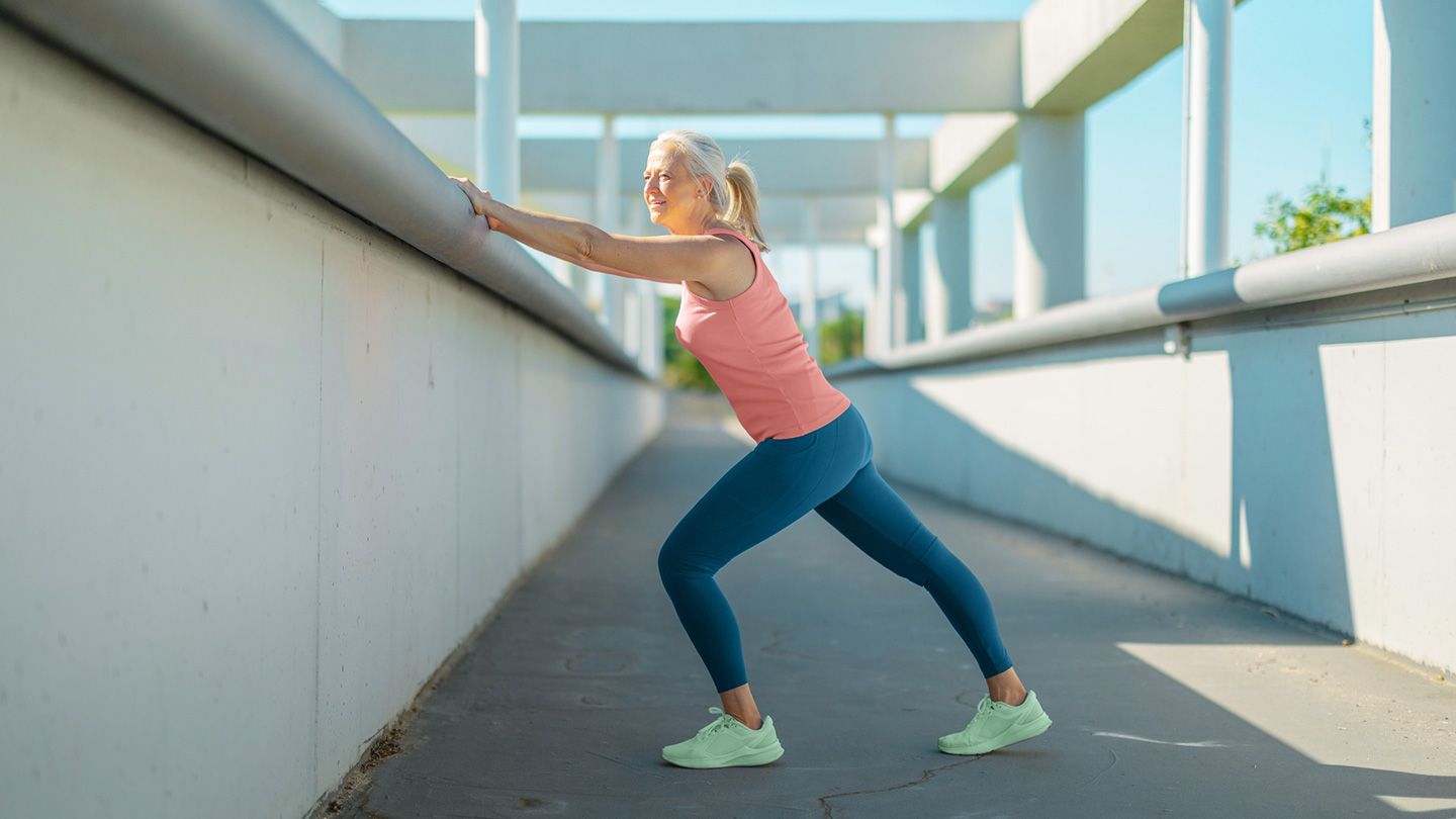 mature woman outside doing wall calf stretch