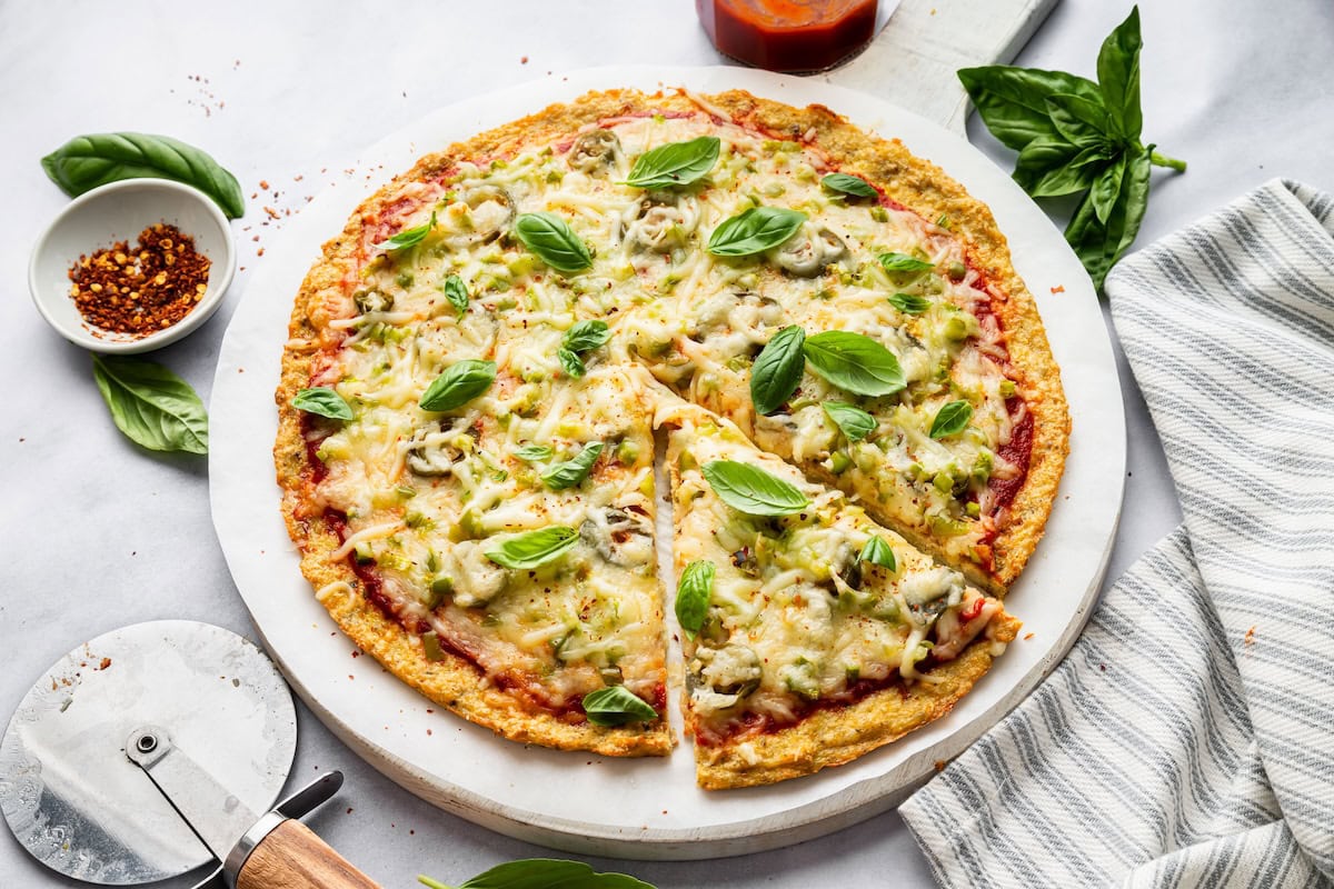 Whole chicken crust pizza topped with fresh basil. One slice has been cut from the crust.