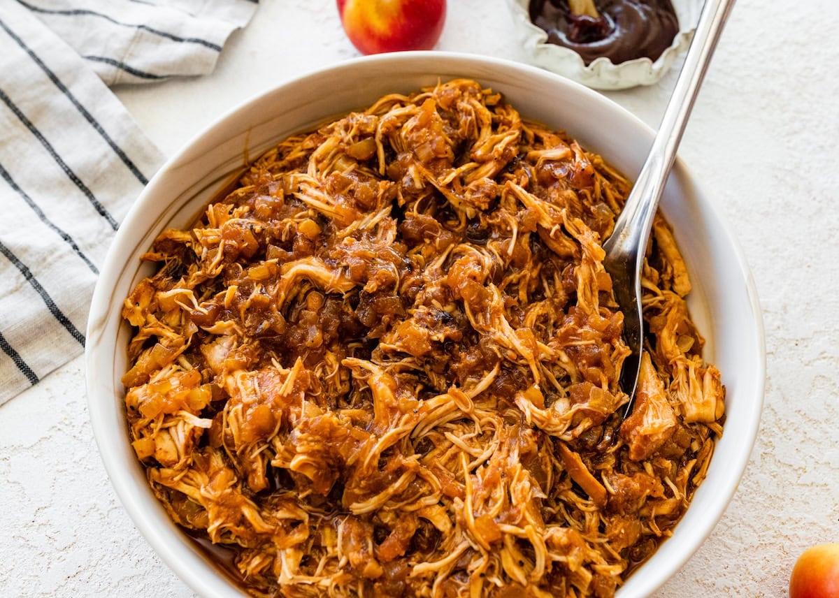 Bowl of shredded apple BBQ chicken with a serving spoon.