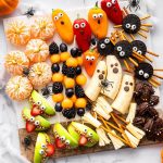 Halloween snack board featuring fruit kabobs, apple monster mouths, banana ghosts, Oreo spiders, and clementine pumpkins.