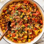 Large skillet filled with cooked ground turkey, vegetables and tomato sauce topped with basil and fresh parmesan cheese. There is a wooden spoon in the mixture.