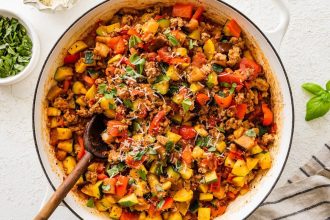 Large skillet filled with cooked ground turkey, vegetables and tomato sauce topped with basil and fresh parmesan cheese. There is a wooden spoon in the mixture.