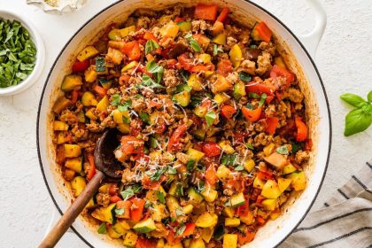 Large skillet filled with cooked ground turkey, vegetables and tomato sauce topped with basil and fresh parmesan cheese. There is a wooden spoon in the mixture.
