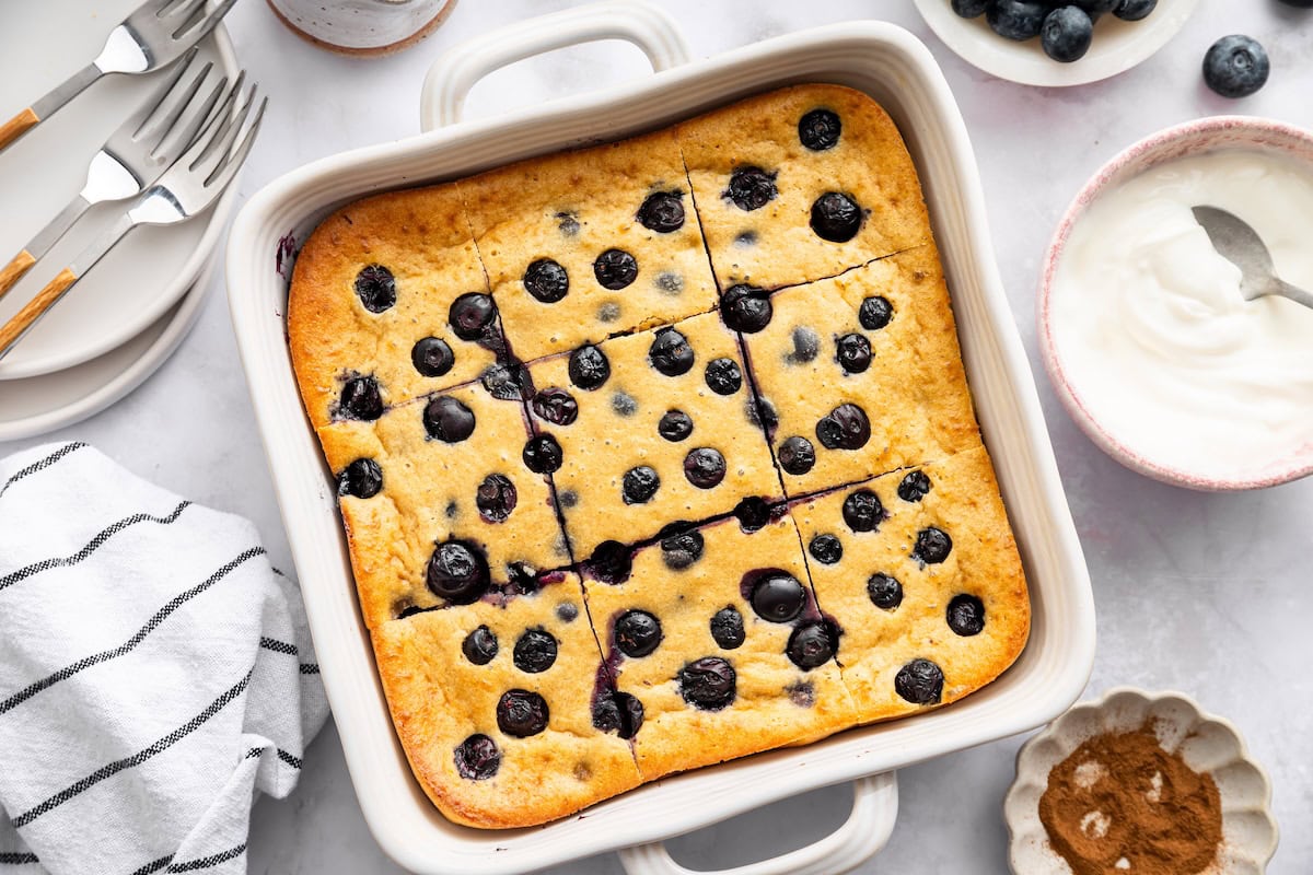 Golden blueberry cottage cheese breakfast bake sliced into pieces in a white ceramic baking pan.
