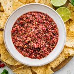Bowl of cranberry salsa surrounded by tortilla chips and lime wedges, ready to serve.