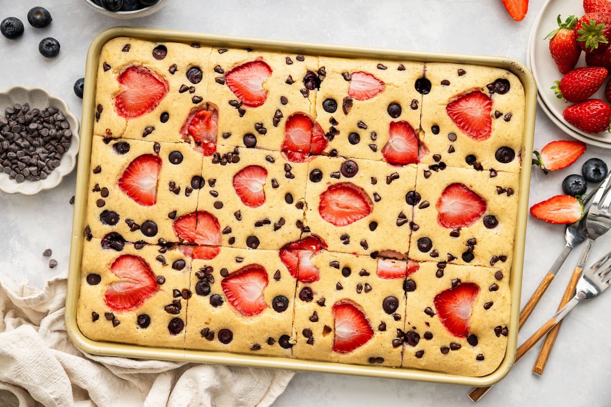 Golden sheet pan pancakes with sliced strawberries and chocolate chips on a baking pan, ready to serve.