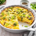 Crustless quiche with broccoli, cheese, onion, and a green onion garnish in a round baking dish with a slice removed.