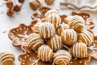 Plate of gingerbread protein balls with white chocolate drizzle arranged on a festive snowflake plate.