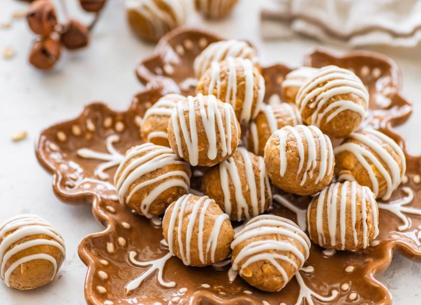 Plate of gingerbread protein balls with white chocolate drizzle arranged on a festive snowflake plate.