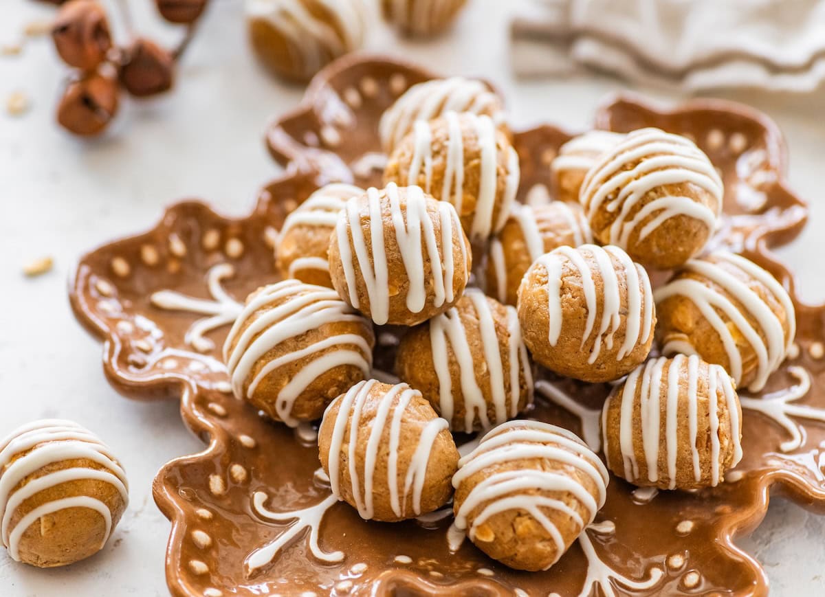Plate of gingerbread protein balls with white chocolate drizzle arranged on a festive snowflake plate.
