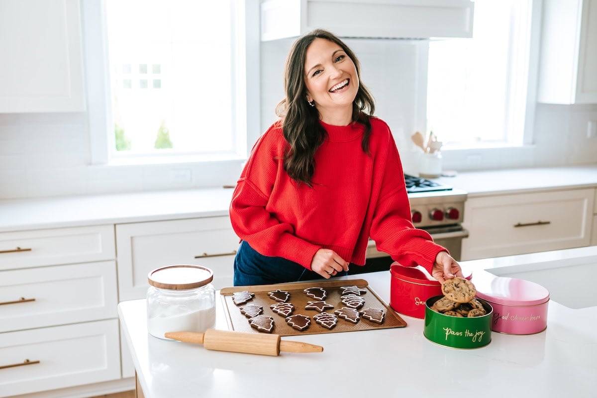 Brittany in a red sweater smiling in the kitchen with a tray of gingerbread cookies in front of her.