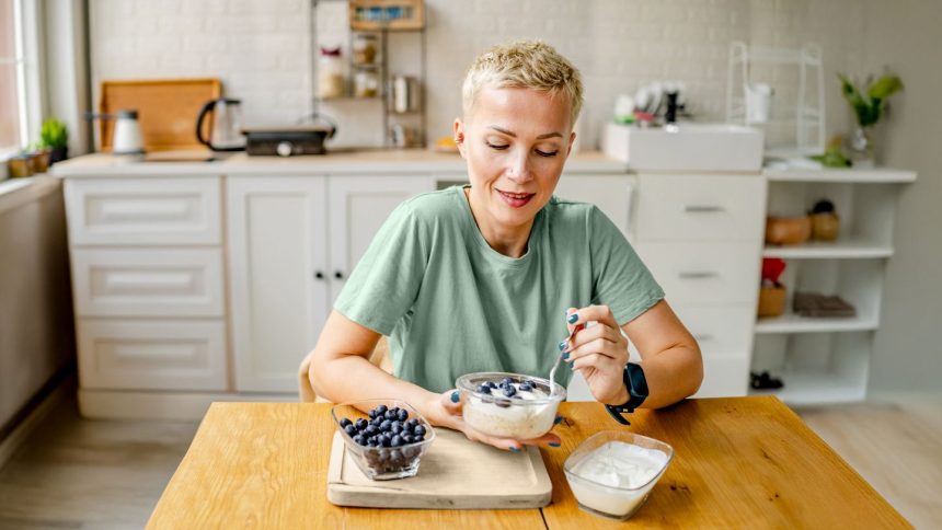 woman eating yogurt with blueberries in kitchen