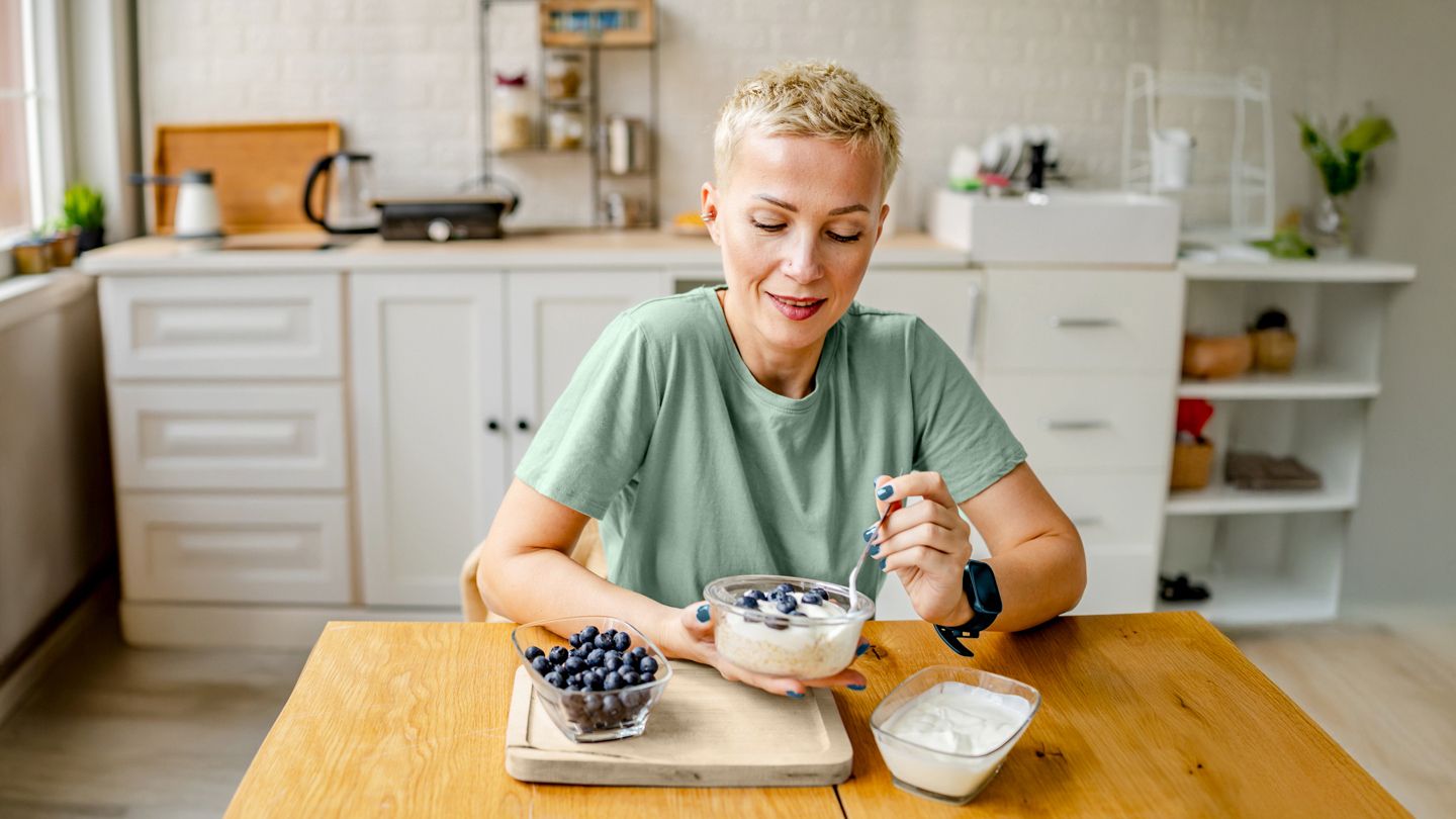 woman eating yogurt with blueberries in kitchen
