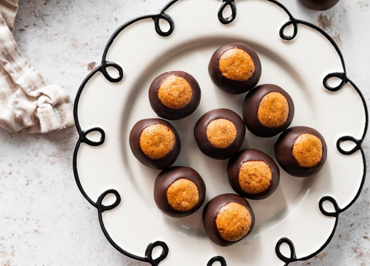Finished high-protein buckeyes displayed on a white decorative plate with chocolate bottoms showing.