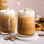 Two iced sugar cookie lattes topped with whipped cream and sprinkles on a holiday-themed table.