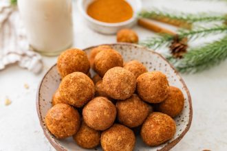 Close-up bowl of snickerdoodle protein balls with cinnamon sugar and milk in the background.