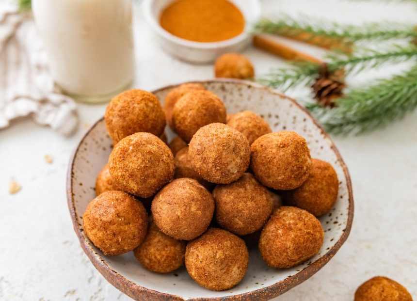 Close-up bowl of snickerdoodle protein balls with cinnamon sugar and milk in the background.