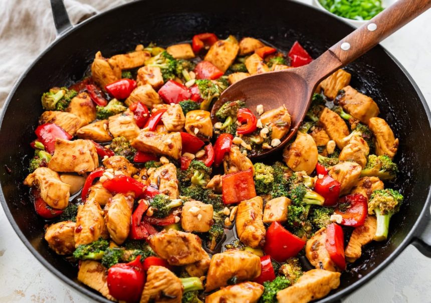 Close-up of kung pao chicken with bell peppers and broccoli being stirred.