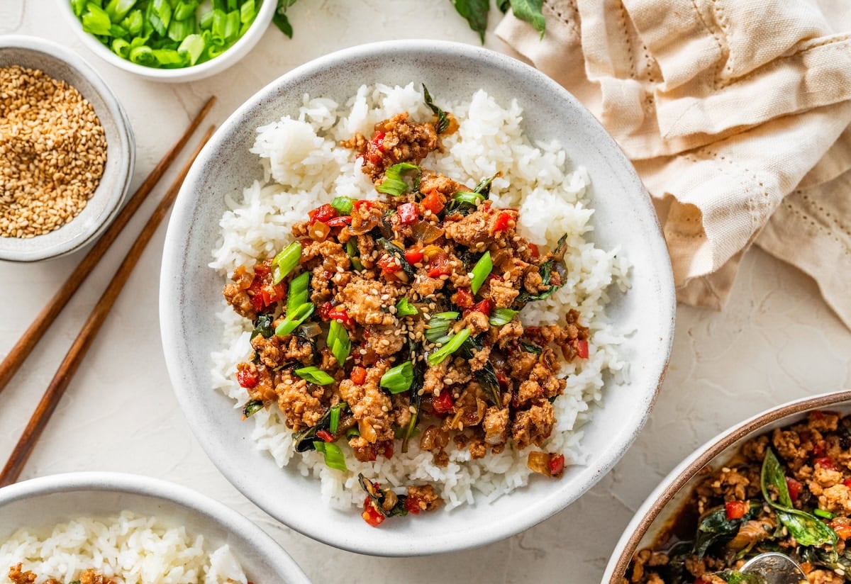 Thai basil chicken spooned over rice with fresh basil and green onions sprinkled on top.