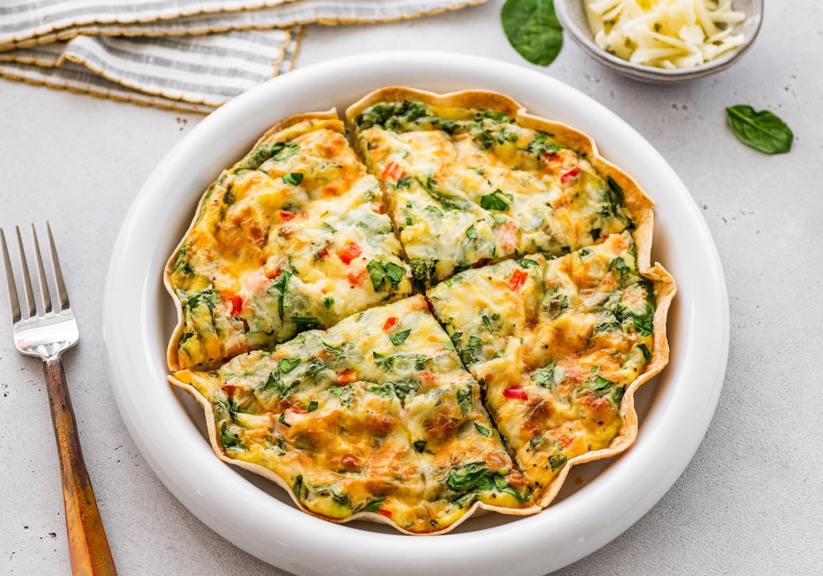 High-protein tortilla quiche sliced into wedges in white pie dish, ready to serve.