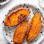 Three oven roasted sweet potato halves on a blue and white speckled plate sprinkled with flaky sea salt.